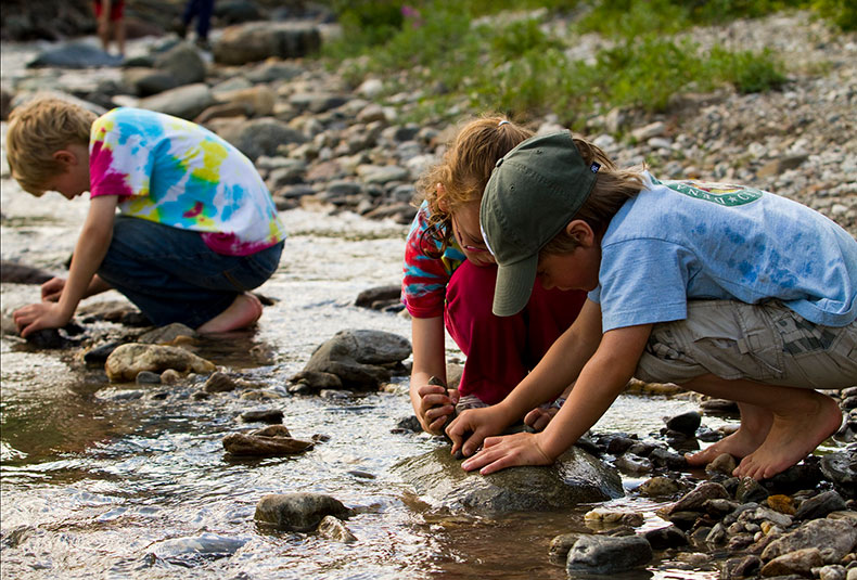 a photo of kids on a beach crouching and looking over sand